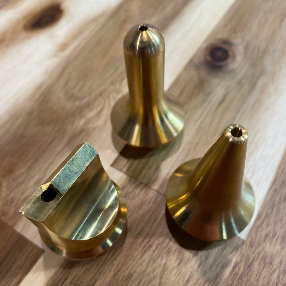 Brass and green cylindrical tool or fastener component with copper cap and small hole, photographed against bright green background